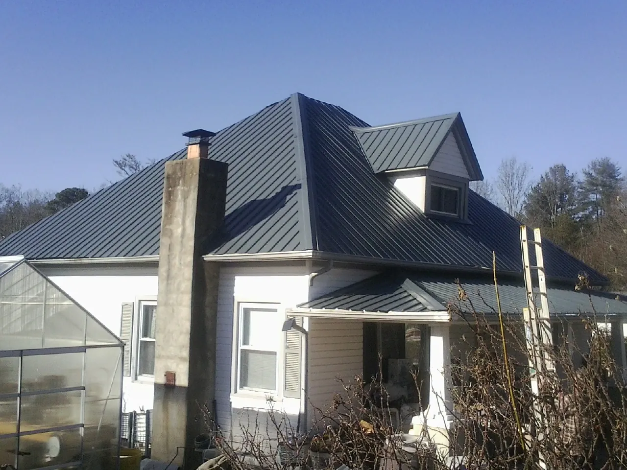 Dark blue standing seam metal roof on a white farmhouse with dormer — Slate & Tile Roof Repair by Roofing Brothers in Leander