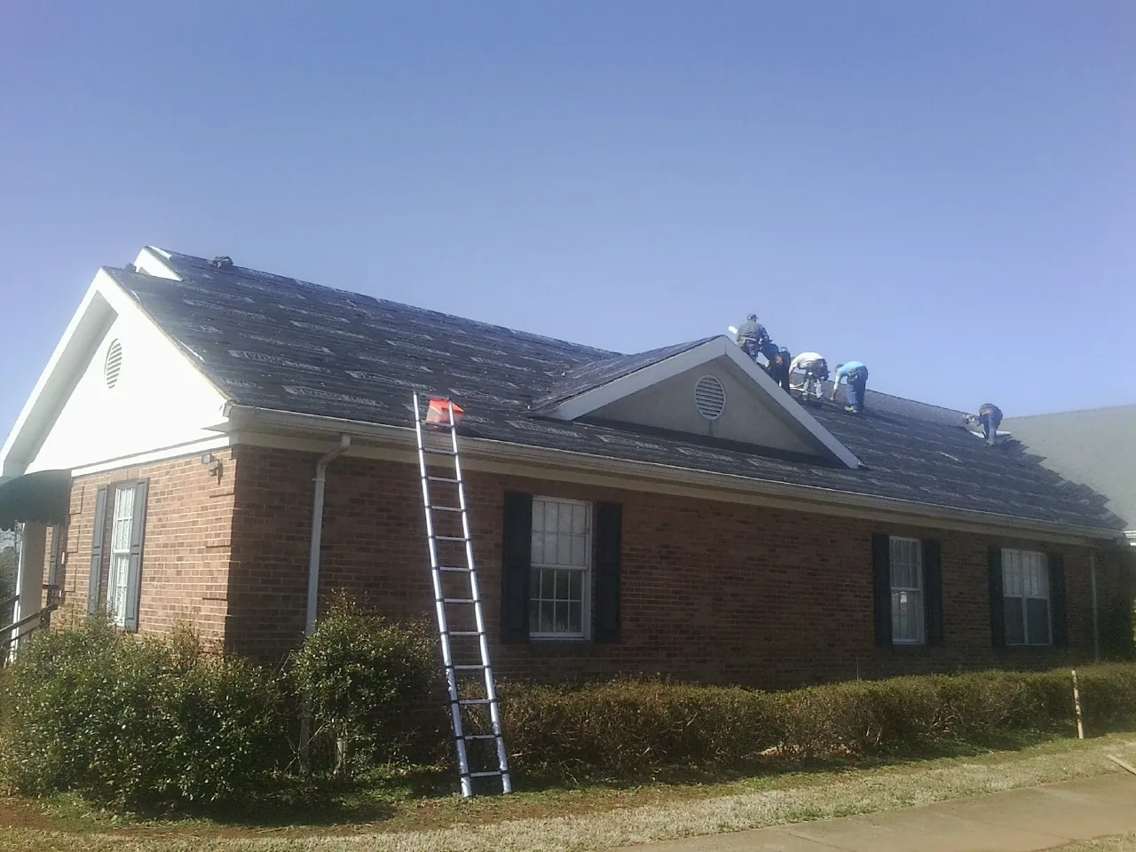 Crew tearing shingles off a brick ranch roof with a ladder set — Emergency Roof Repair work by our crew in Leander