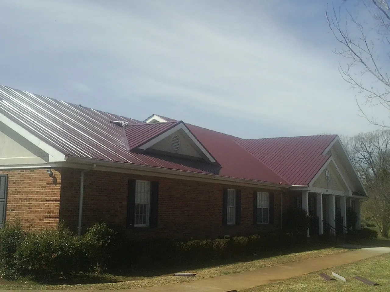 Red metal roof with gabled entries on a long brick building, from a Hail Damage Roof Repair job in Leander