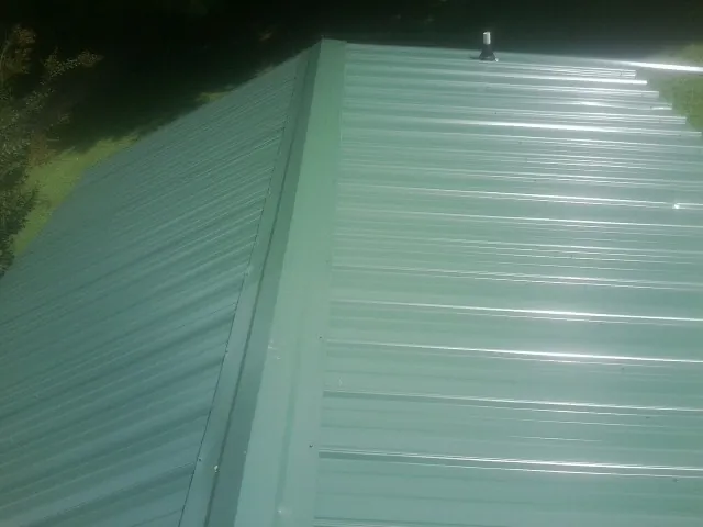 New green metal panels meeting at the ridge of a roof — Flat Roof Repair work by our crew in Leander