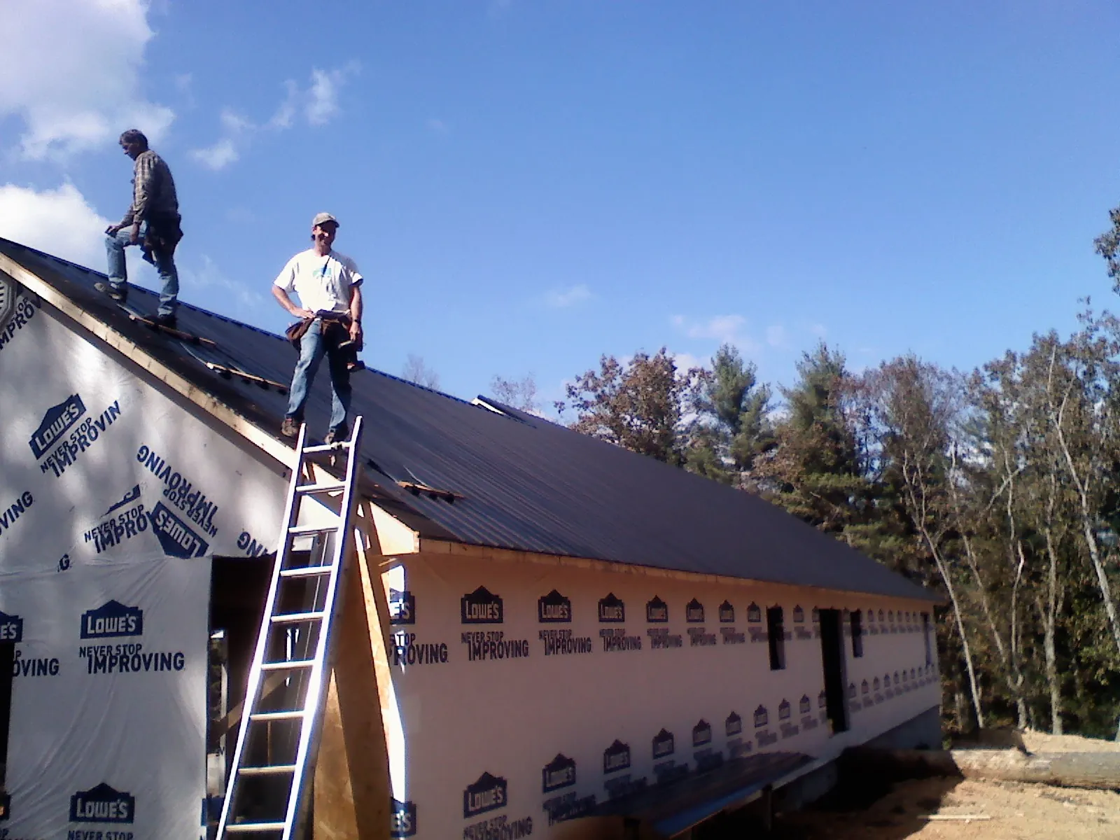 Two roofers standing on a long dark metal roof over a wrapped building in Leander